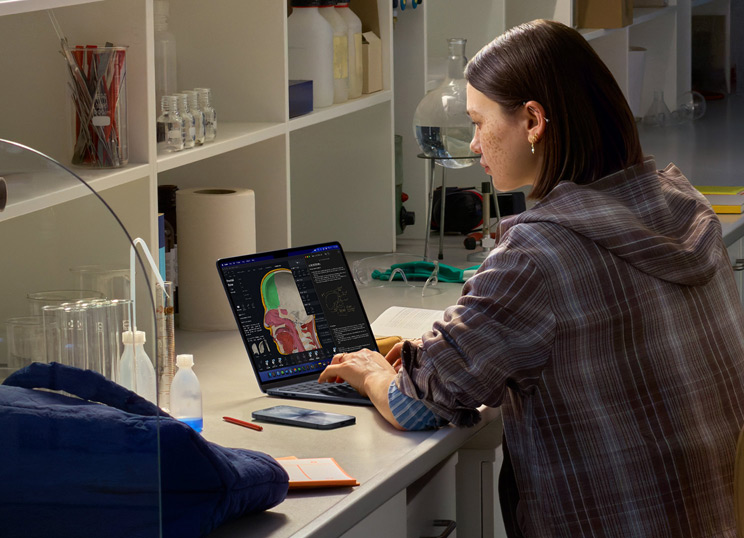 Uma pessoa sentada num laboratório a usar o MacBook, com o ecrã a mostrar várias apps.