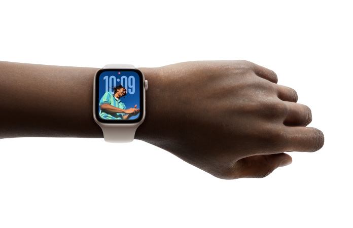 特寫畫面顯示手腕上戴著配上橡膠錶帶的銀色 Apple Watch，展示全新 Liquid Glass 設計的時鐘 app