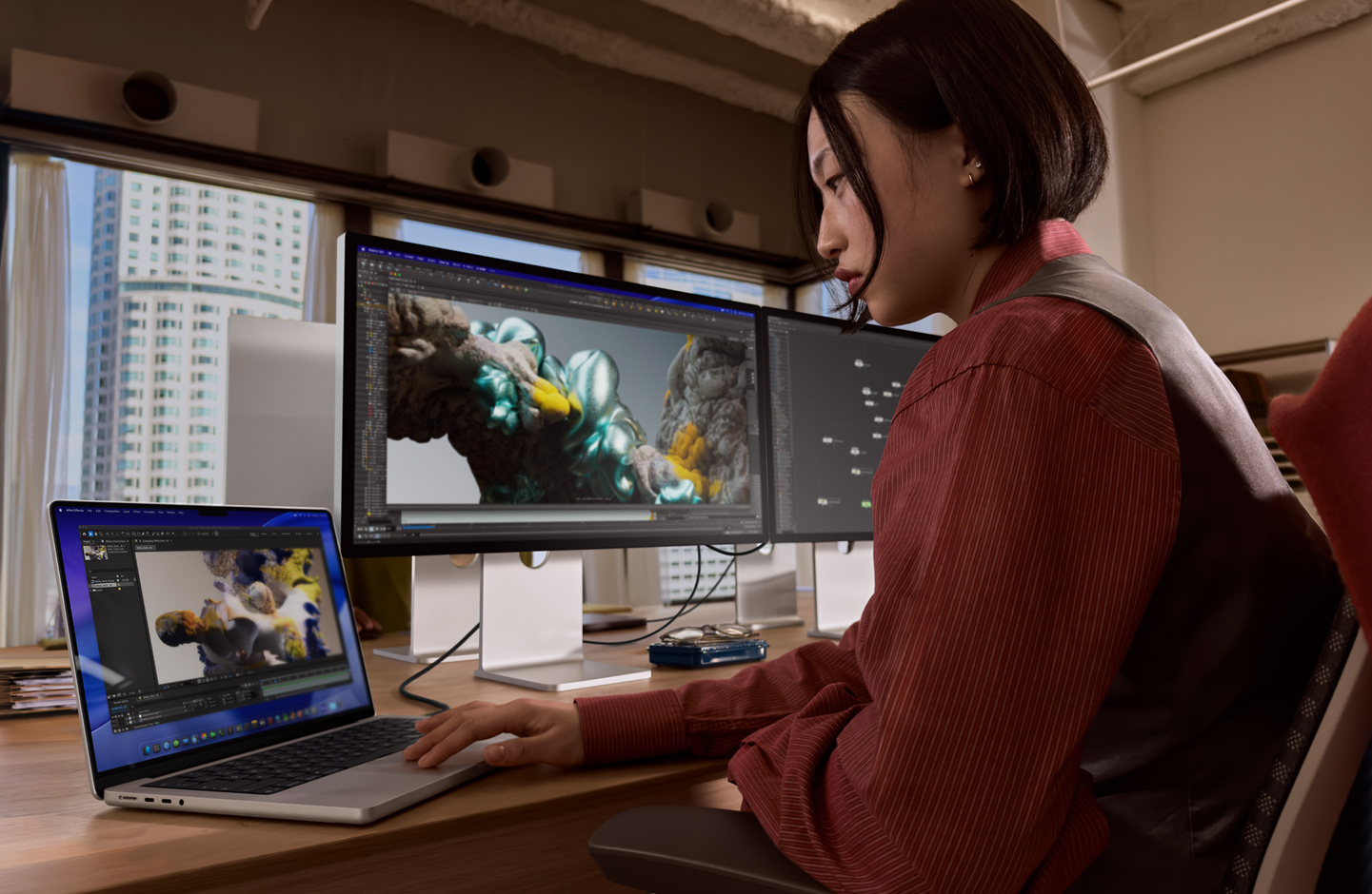 O persoană într-un cadru de birou lucrează pe un laptop MacBook care este conectat la Studio Display XDR printr-un port Thunderbolt 5